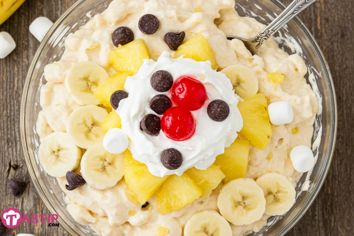 Banana Split Fluff dessert served in a bowl with bananas, marshmallows, and whipped topping, garnished with chocolate chips and maraschino cherries